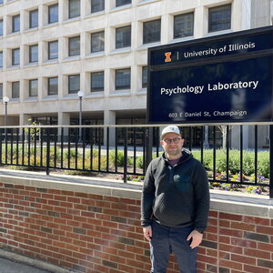 Benedek Kurdi in front of a sign saying “Psychology Laboratory” at the University of Illinois Psychology Department building.